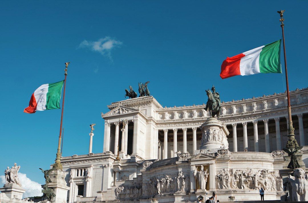 Bandiera italiana sventola davanti a un edificio monumentale, simbolo della denuncia di Ancodis sull'incostituzionalità del CCNL scolastico e del sistema retributivo basato sull'anzianità.
