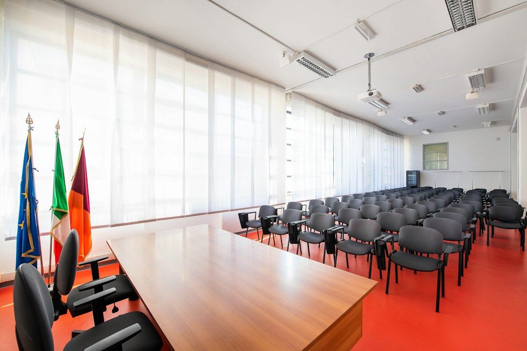Aula conferenze con sedie e bandiere, sfondo della condanna a 270mila euro per docente con attività privata incompatibile