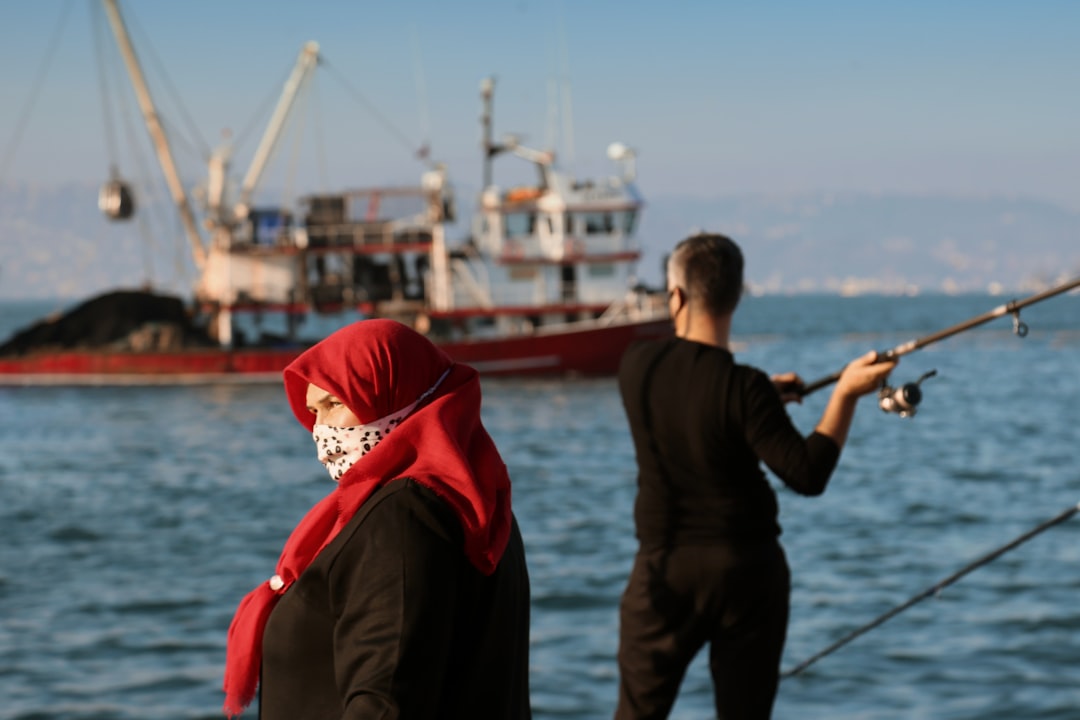 Donna con hijab rosso e mascherina, pescatore e nave sullo sfondo, simbolo di solidarietà e sostegno a Gaza e alla Flotilla.
