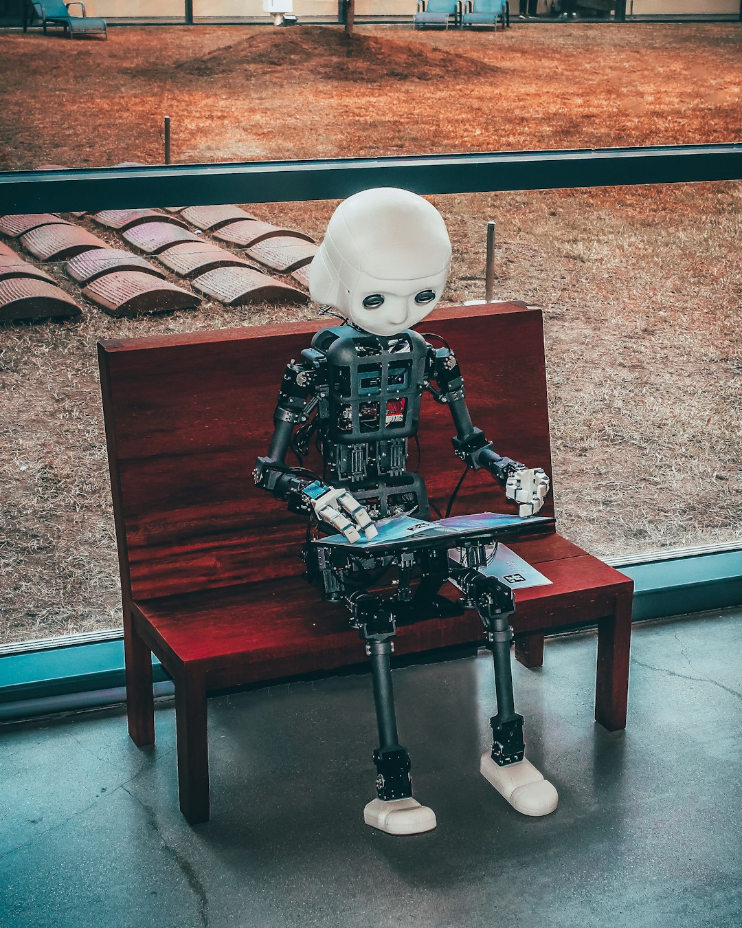 Un robot umanoide seduto su una panca rossa legge un libro, simbolo dell'apprendimento nell'era dell'intelligenza artificiale e del futuro dell'istruzione.