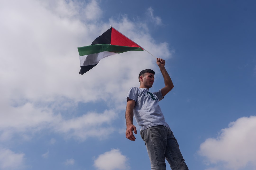 Giovane attivista sventola bandiera palestinese contro cielo azzurro, simbolo della nuova generazione di attivisti per Gaza.