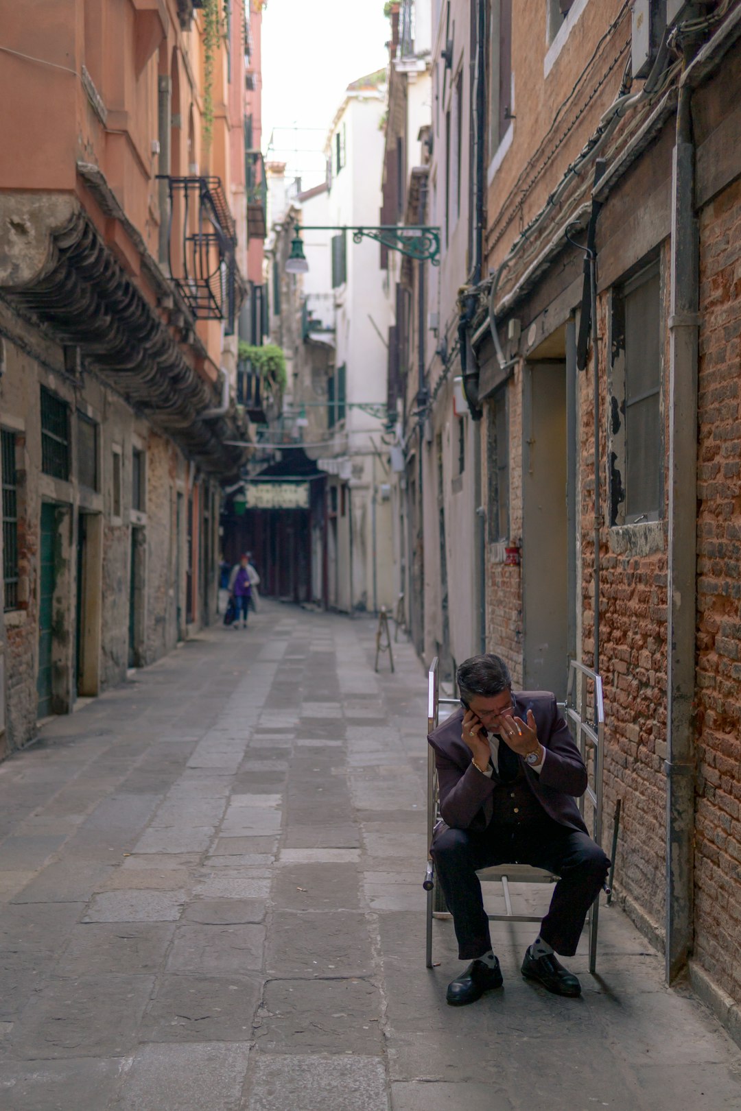 Uomo pensieroso al telefono in una calle veneziana, metafora della solitudine e benessere mentale giovanile in Italia