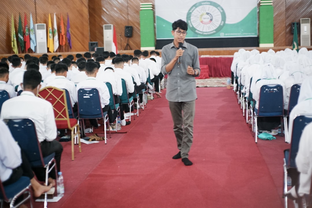 Giovane uomo con microfono parla a un pubblico seduto in un'aula, contesto istruzione adulti e maturità