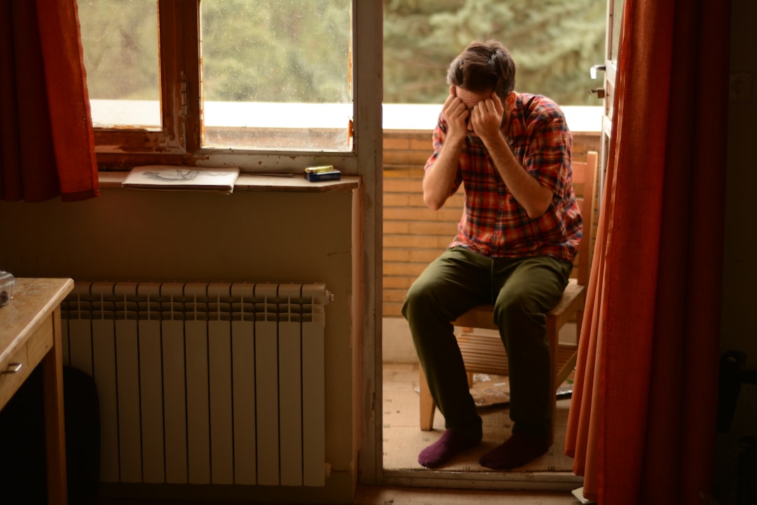 Uomo seduto con le mani sul viso, espressione di stress e burnout, in un contesto domestico che suggerisce isolamento e difficoltà emotive.