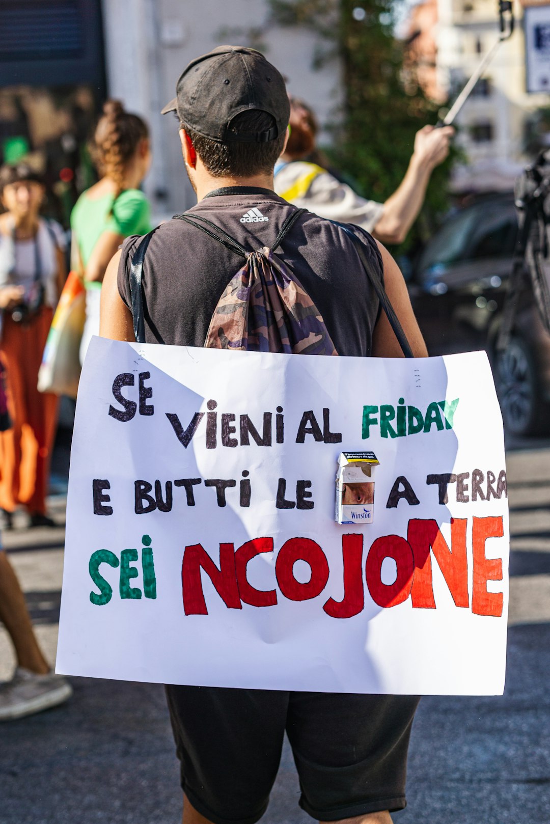 Manifestazione a Milano contro l'esclusione scolastica: cartello con slogan provocatorio e pacchetto di sigarette, sciopero del 22 settembre.