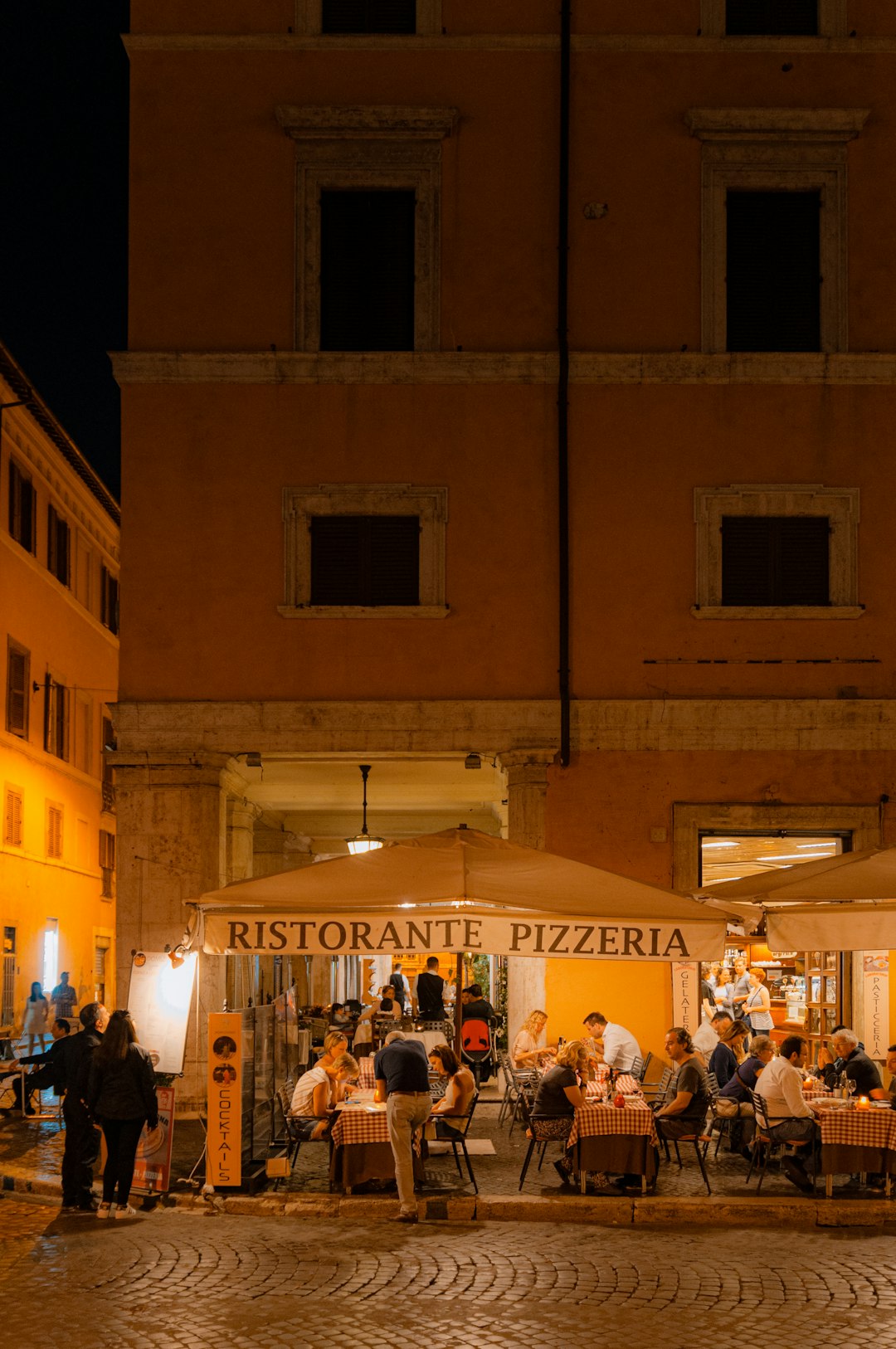 Ristorante pizzeria illuminato di sera a Roma, atmosfera conviviale durante la Notte dei Ricercatori e delle Ricercatrici 2023.