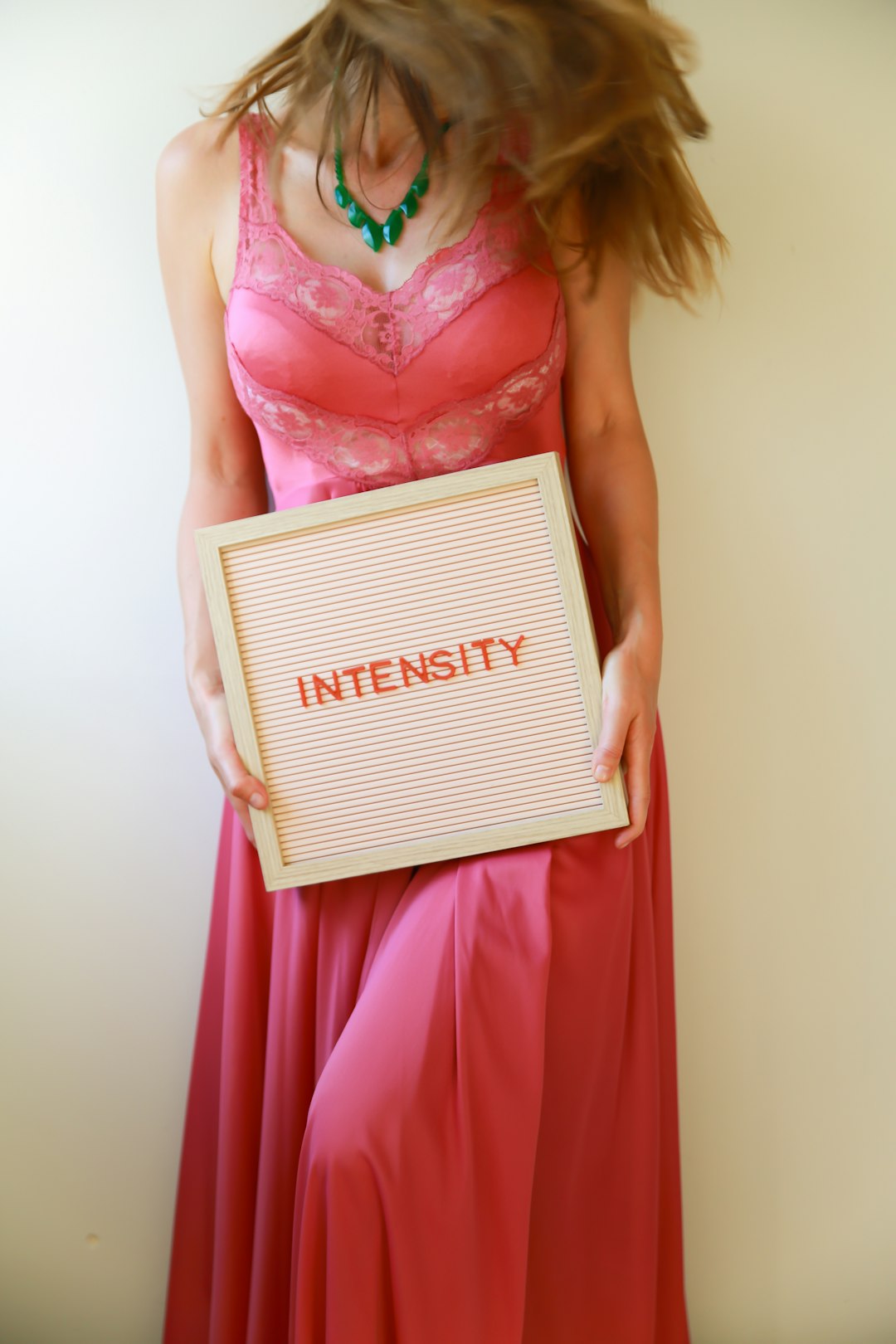 Donna con abito rosa che mostra una lavagna con la scritta Intensity, simbolo di una vita vissuta con intensità e consapevolezza.
