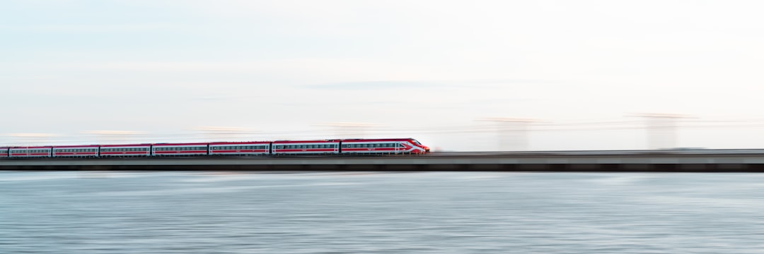 Treno ad alta velocità rosso e bianco su ponte ferroviario sull'acqua, simbolo di viaggi Interrail e Trenitalia in Europa.